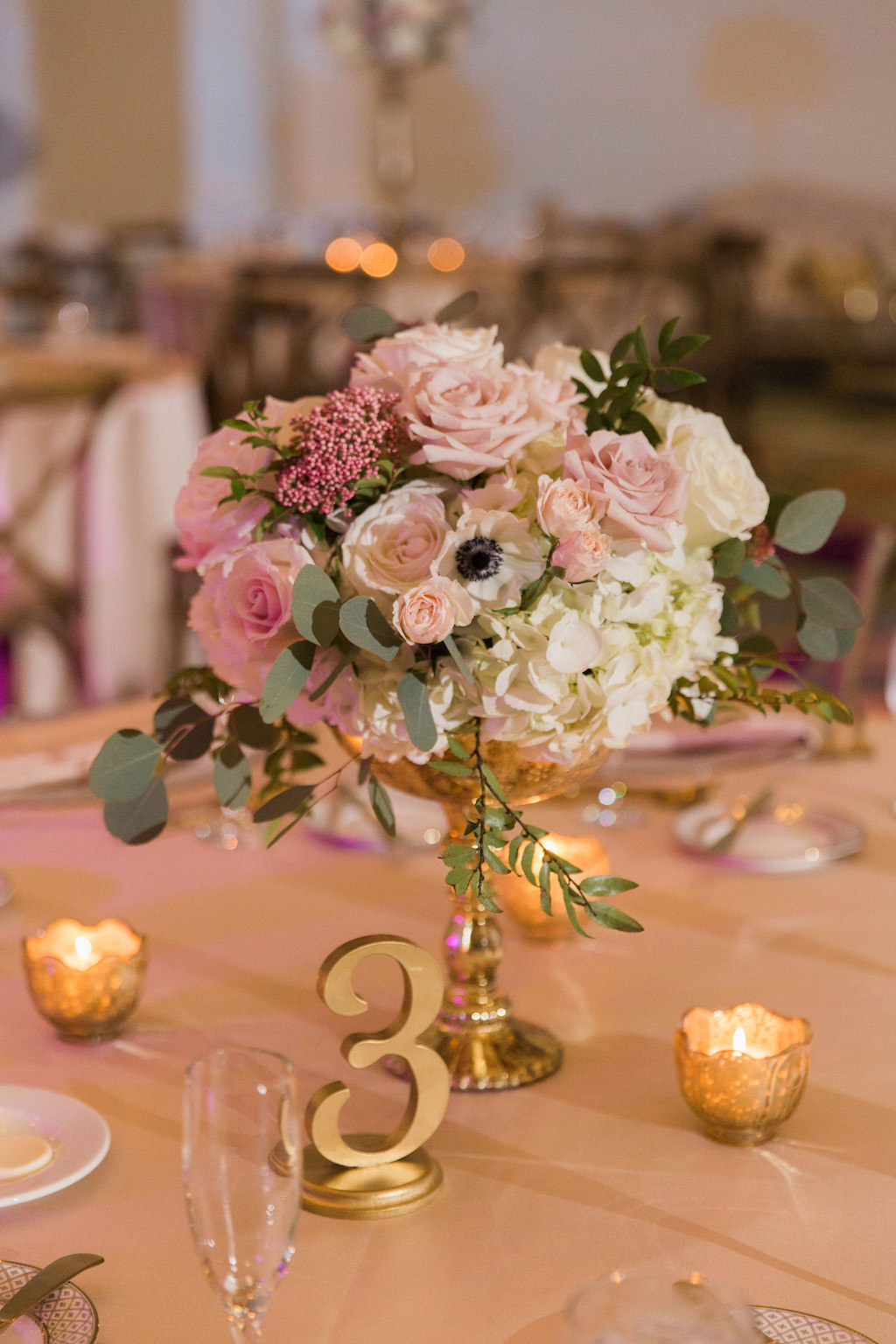 Low Pink Rose and White Anemone Centerpiece with Greenery in Gold Vase with Blush Pink Linens and Gold Votive Candle Holders and Stylish Gold Table Number | Tampa Bay Event Planner Parties A La Carte