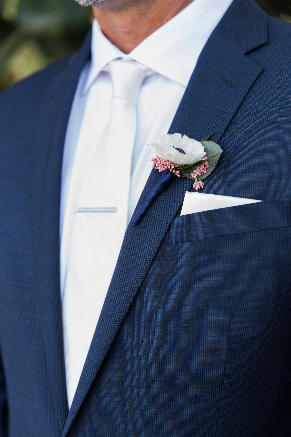 Groom with White Anemone and Pink Blossom Ribbon Wrapped Boutonniere, White Silk Tie, and Navy Suit