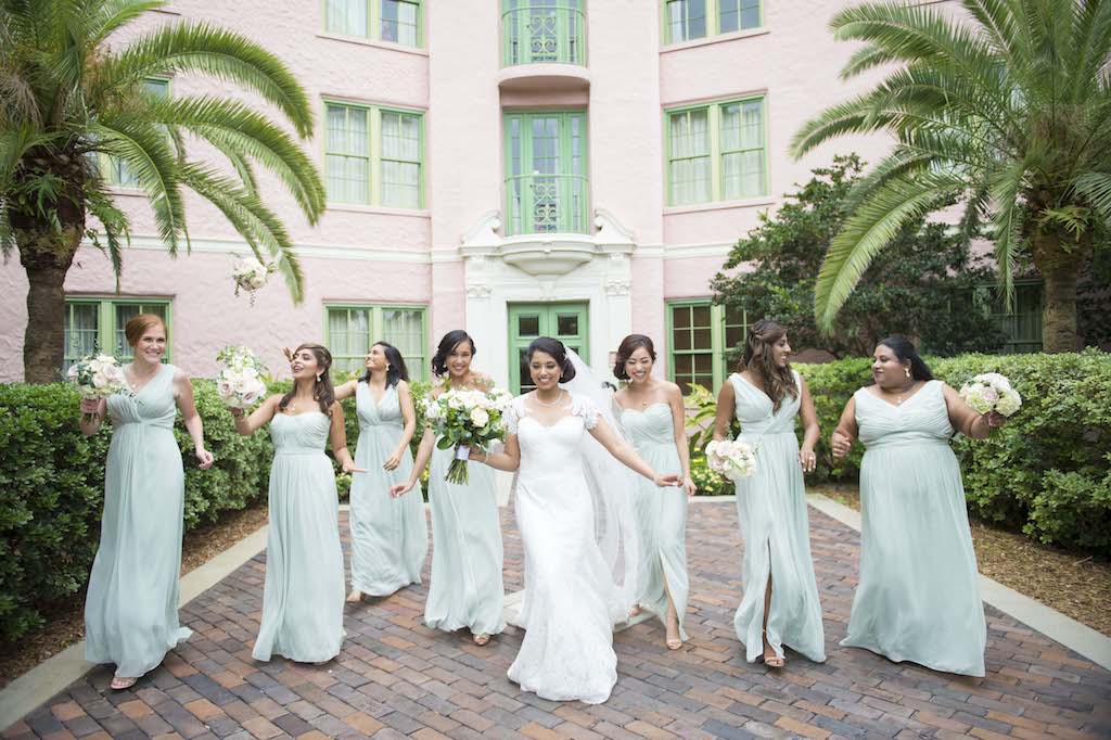 Outdoor Garden Bridal Party Portrait with Green Lace Shoulder Augusta Jones Wedding Dress, White Floral Bouquet with Greenery, and Mismatched Sage Green Dessy Group Bridesmaids Dresses | St. Pete Historic Hotel Wedding Venue The Vinoy Renaissance