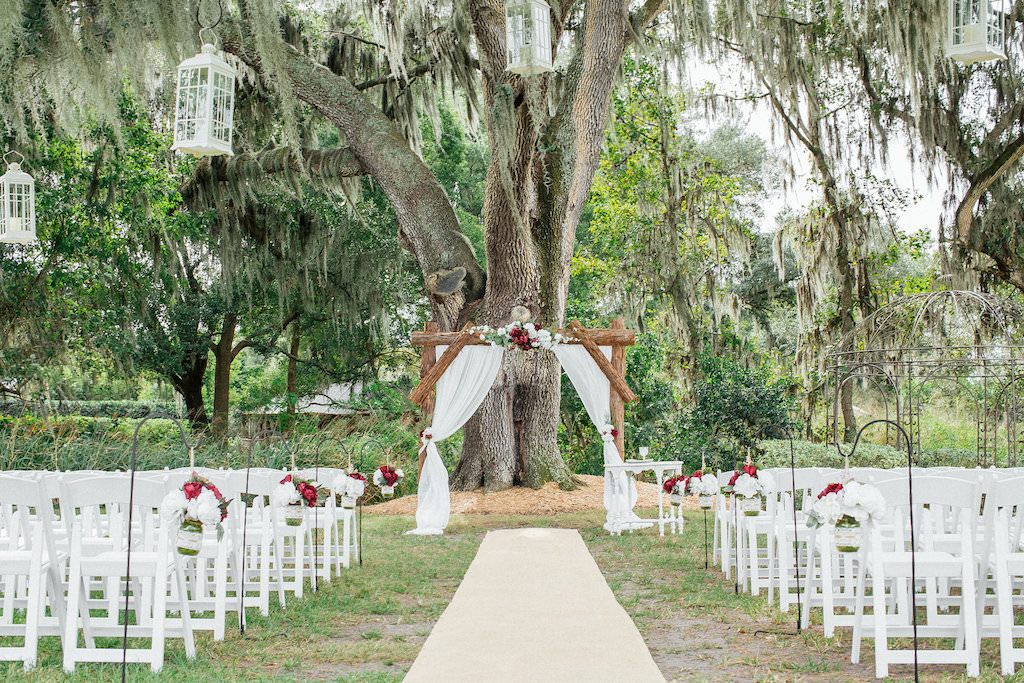 Rustic White and Burgundy Farm Wedding Outdoor Ceremony with Wooden Arch with Drapery, Hanging Mason Jar Flowers, White Folding Chairs, Hanging Lanterns, and Burlap Aisle | Tampa Bay Wedding Venue Cross Creek Ranch