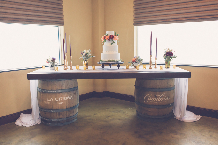 Modern Rustic Wedding Dessert Table on Antique Barrels, with 4 Tier Round White Wedding Cake with Peach and Bordeaux Roses with Greenery, with Tall Burgundy Candles in Gold Candleholders, and Peach and Red Flowers with Sage Greenery in Gold Geodesic Vases | Tampa Bay Wedding Reception Venue Crowne Plaza Tampa