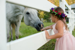 Outdoor Rustic Wedding Portrait of Flower Girl with Horse, wearing Blush Pink Dress and Purple, Red, and Pink Floral Crown with Greenery | Tampa Bay Wedding Photographer Caroline & Evan Photography | Outdoor Wedding Venue Southern Plantation Oasis