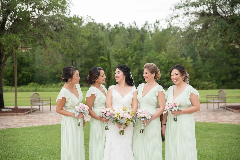 Outdoor Garden Bridal Party Portrait with V Neck Stella York Wedding Dress, Light Green V Neck Bridesmaids Dresses with Flutter Sleeves, and Pink, White, and Yellow Bouquets with Greenery and Green Ribbon | Vietnamese Inspired Tampa Bay Wedding | Tampa Wedding Photographer Kristen Marie Photography