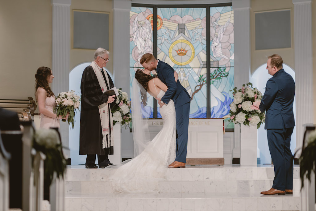 Traditional Church Wedding Ceremony First Kiss Portrait, Groom in Navy Suit, Floral Decor with Large White Hydrangeas, Blush Roses and Greenery on White Pillars | St Pete Wedding Venue Northeast Presbyterian Church