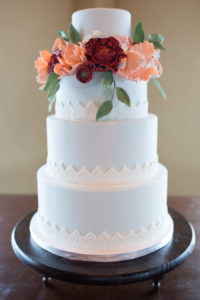 Four Tiered Round Light Blue with Triangle Lace Pattern Wedding Cake on Dark Wood Cake Stangd, with Peach and Burgundy Rose with Greenery Flowers