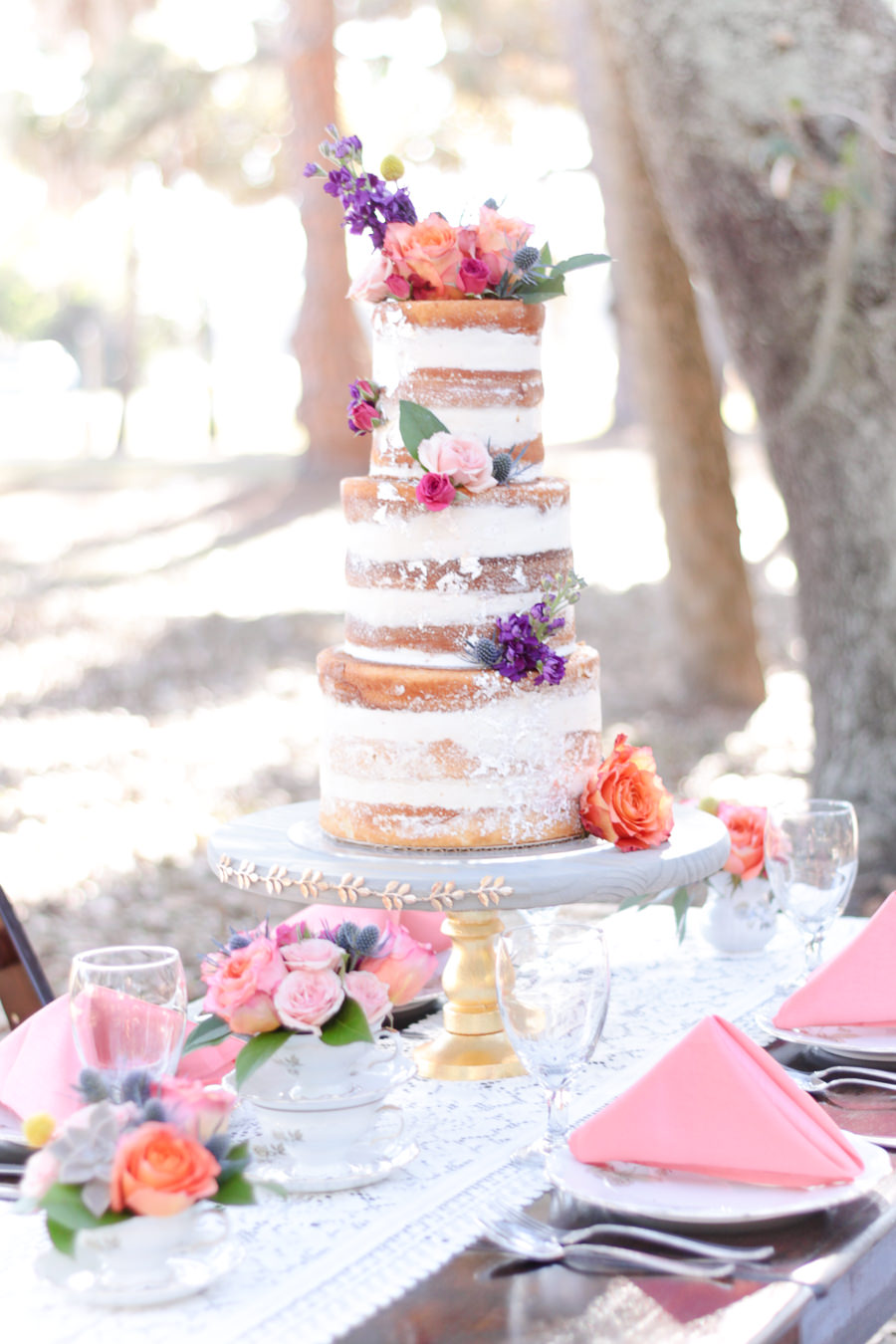 Outdoor Park Wedding Reception with Three Tier Round Naked Wedding Cake with Tropical Flowers, Table Decor with Lace Runner, Low Blush, Peach, Thistle and Succulent with Greenery Centerpiece, and Coral Napkins