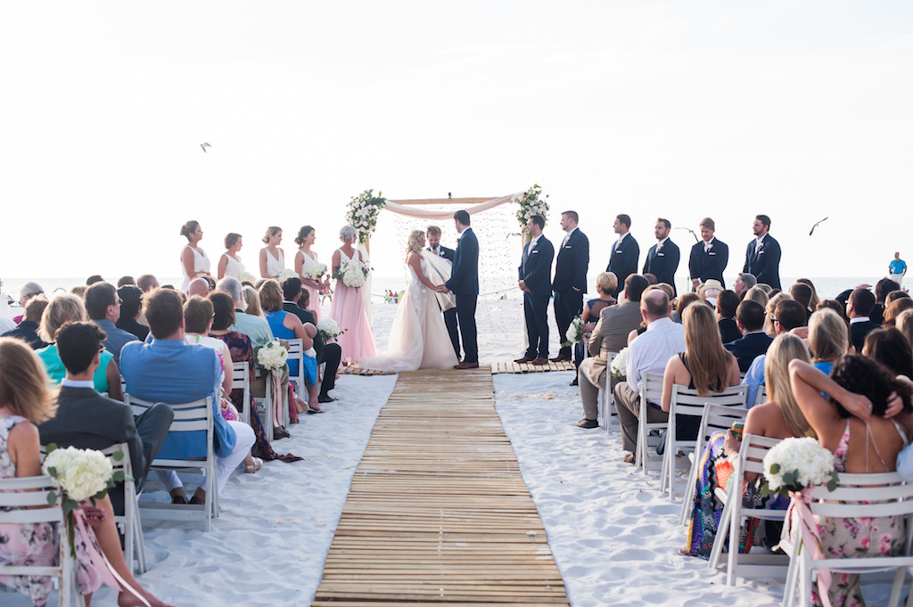 Boho Florida Beach Wedding Ceremony with Bamboo Ceremony Aisle, White Folding Chairs with Hydrangeas and Blush Ribbon, and Floral Bamboo Arch, Groomsmen in Navy Suits | Destination Hotel Wedding Venue Hilton Clearwater Beach