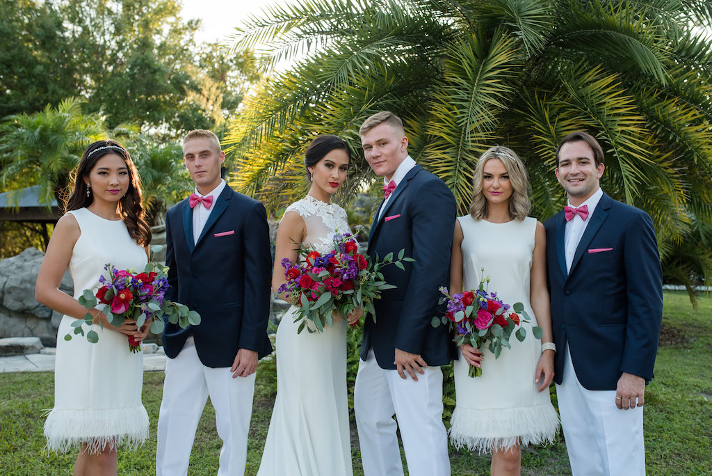 Retro Inspired Southern Wedding Bridal Party Portrait, Bridesmaids in Knee-length White Dresses with Feathers, Bride in Lace Cutout A Line Wedding Dress from Tampa Bridal Dress Shop The Bride Tampa | Groomsmen in Navy Blue Jackets with Pink Bow Ties and White Pants | Bridesmaids Dresses from Truly Forever Bridal | Tampa Wedding Flowers Northside Florist | Tampa Bay Wedding Photographer Caroline & Evan Photography | Tampa Bay Wedding Planner Exquisite Events