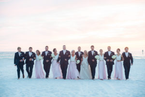 Outdoor Boho Beach Wedding Party Portrait, Bride in Lace Floral Monique Lhuillier, Bridesmaids in Two Piece White V Neck Crop Tops and Long Pink Skirts, and Groomsmen in Navy Blue Suits with Blush Pink Ties | Destination Hotel Wedding Venue Hilton Clearwater Beach