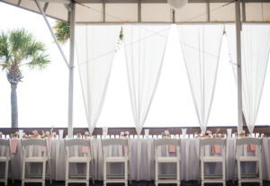 Boho Beach Wedding Hotel Reception with White Drapery, Blush Napkins, and Small White Floral and Natural Driftwood Centerpiece, and White Folding Chairs | Tampa Bay Florida Beach Destination Hotel Wedding Venue Hilton Clearwater Resort & Spa