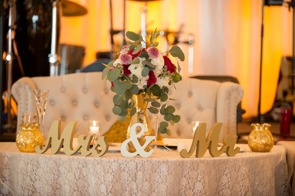 Old Florida Theme Wedding Reception Sweetheart Table with Vintage Couch, Floral Linens, and Stylish Gold Mr and Mrs Sign, and Medium Height Pink, White, and Red Rose with Greenery Centerpiece | Tampa Wedding Rentals Connie Duglin Linens