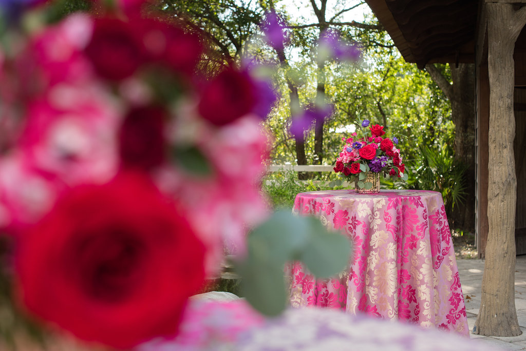 Colorful Outdoor Wedding Cocktail Reception Decor with Centerpieces with Red Roses, Pink, and Purple Flowers and Greenery on Pink and Gold Paisley Table Cloths | Northside Florist | Over the Top Rental Linens