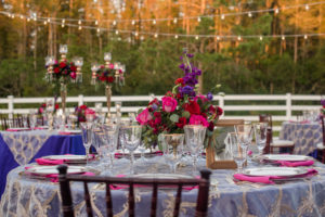 Elegant Southern Outdoor Wedding Reception Table Decor with Navy Blue, Vintage Lace, and Magenta Linens, Tall Gold Candelabra Centerpieces with Hurricane Lanterns, Red and Pink Roses, Purple Flowers and Greenery | Tampa Bay Wedding Planner Exquisite Events | Outdoor Tampa Bay Wedding Venue Southern Plantation Oasis | Northside Florist | Rentals by A Chair Affair