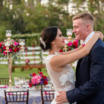 Luxurious Outdoor Tampa Bay Wedding Reception First Dance Portrait, with Navy Blue Linens, and Tall Gold Candelabra Centerpieces with Red, Magenta, and Purple Florals with Greenery | Tampa Wedding Photographer Caroline & Evan Photography | Tampa Bay Wedding Planner Exquisite Events