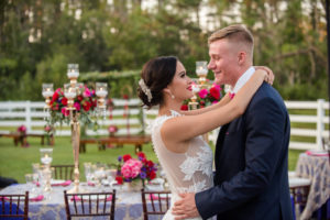 Luxurious Outdoor Tampa Bay Wedding Reception First Dance Portrait, with Navy Blue Linens, and Tall Gold Candelabra Centerpieces with Red, Magenta, and Purple Florals with Greenery | Tampa Wedding Photographer Caroline & Evan Photography | Tampa Bay Wedding Planner Exquisite Events
