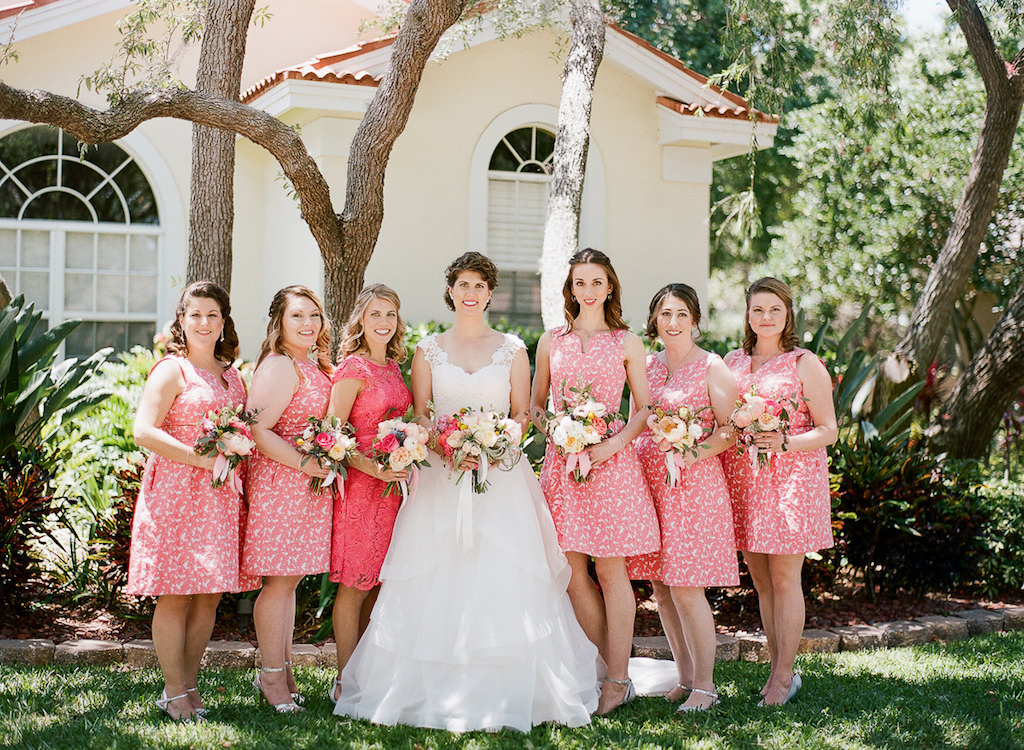 Outdoor Garden Bridal Party Portrait with Cream, Pink Rose and Floral and Greenery Bouquets, Bride in V Neck A Line Paloma Blanca Wedding Dress, Bridesmaids in Coral Floral Knee Length Adrianna Papell Dresses with Strappy Silver Shoes