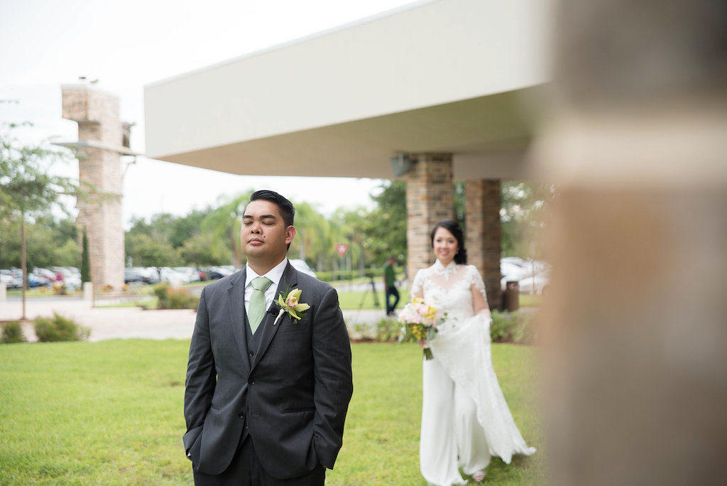 Outdoor First Look Bride and Groom Portrait, Bride in Long Sleeve High Collar Traditional Vietnamese Ao Dai Wedding Dress with Pink and Yellow and Greenery Bouquet, Groom with Yellow Boutonnière in Gray Three Piece Suit with Light Green Tie | Tampa Bay Wedding Photographer Kristen Marie Photography