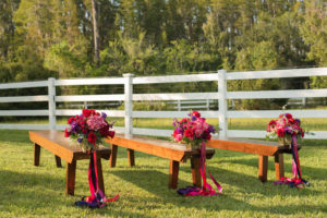 Outdoor Rustic Wedding Ceremony Decor with Wooden Benches, and Small Red, Purple, and Magenta Flowers with Pink and Purple Ribbon | Tampa Bay, Florida Wedding Venue Southern Plantation Oasis | Northside Florist