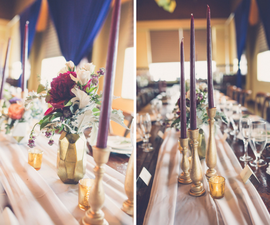 Elegant Modern Rustic Wedding Reception Table Decor with Tall Bordeaux Candles in Gold Candlestick Holders, Blush Table Runner, and small Magenta and White Floral with Greenery Centerpiece in Geodesic Gold Vase, Navy Blue Draping