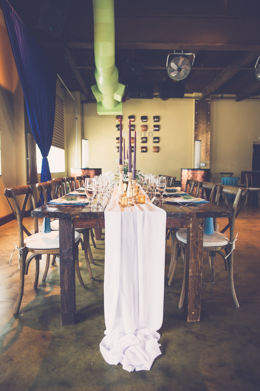 Boho Wedding Reception with Wooden Table, Wood X Back Chairs, Tall Burgundy Candles, Gold Accents, and Navy Blue Drapery | Tampa Bay Hotel Wedding Reception Venue Crowne Plaza Tampa | Tampa Farm Table Rentals A Chair Affair