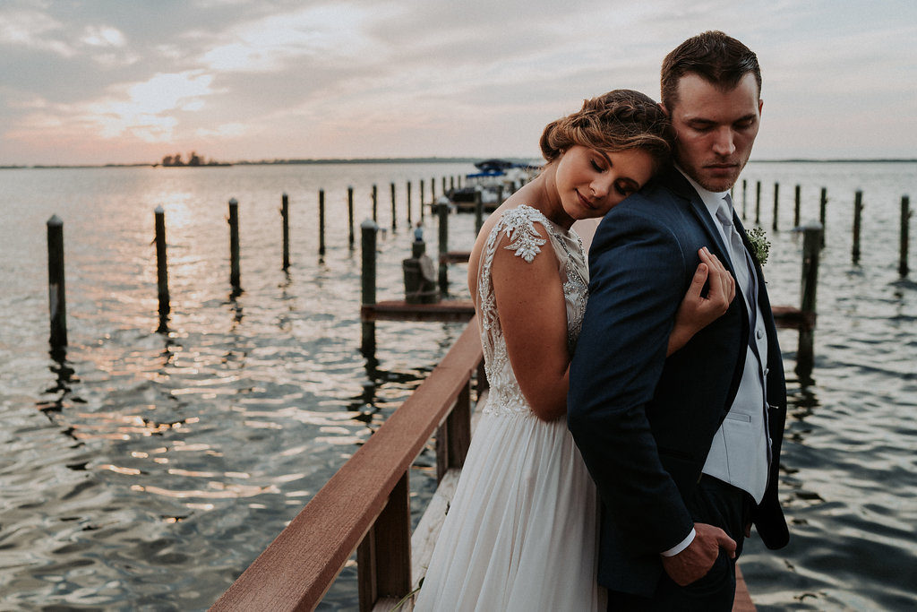 Outdoor Portrait on Waterfront Dock, Bride wearing Jeweled Lace Drop Back A Line Wedding Dress, Groom in Navy Suit with Silver Vest from Tampa Bay Formalwear Shop Nikki's Glitz and Glam | Dunedin, Florida Waterfront Wedding Venue Beso Del Sol Resort | Tampa Bay Wedding Photographer Grind and Press Photography | Hair and Makeup Femme Akoi