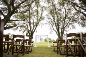 Outdoor Wedding Ceremony Decor with Arch with White Drapery and Hanging Greenery Garlands with Red Roses and White Flowers and Wooden Folding Chairs | Clearwater Golf Course Wedding Venue Countryside Country Club | Planner Special Moments Event Planning | Florist & Draping Gabro Event Services