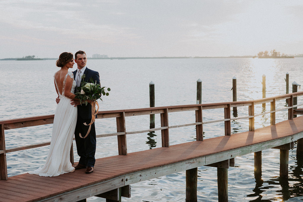 Outdoor Portrait on Waterfront Dock, Bride wearing Jeweled Lace Drop Back A Line Wedding Dress, Groom in Navy Suit with Silver Vest from Tampa Bay Formalwear Shop Nikki's Glitz and Glam | Dunedin, Florida Waterfront Wedding Venue Beso Del Sol Resort | Tampa Bay Wedding Photographer Grind and Press Photography