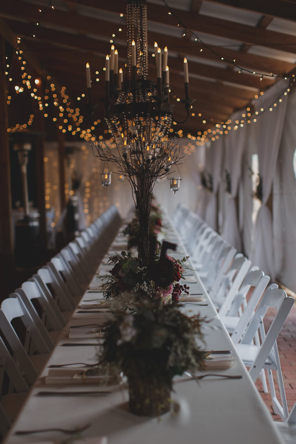 Rustic Barn Wedding Reception with Long White Feasting Table with Natural Greenery Small Centerpieces and Folding White Chairs, Hanging Candelabras and String Lights | Tampa Bay Wedding Venue Cross Creek Ranch
