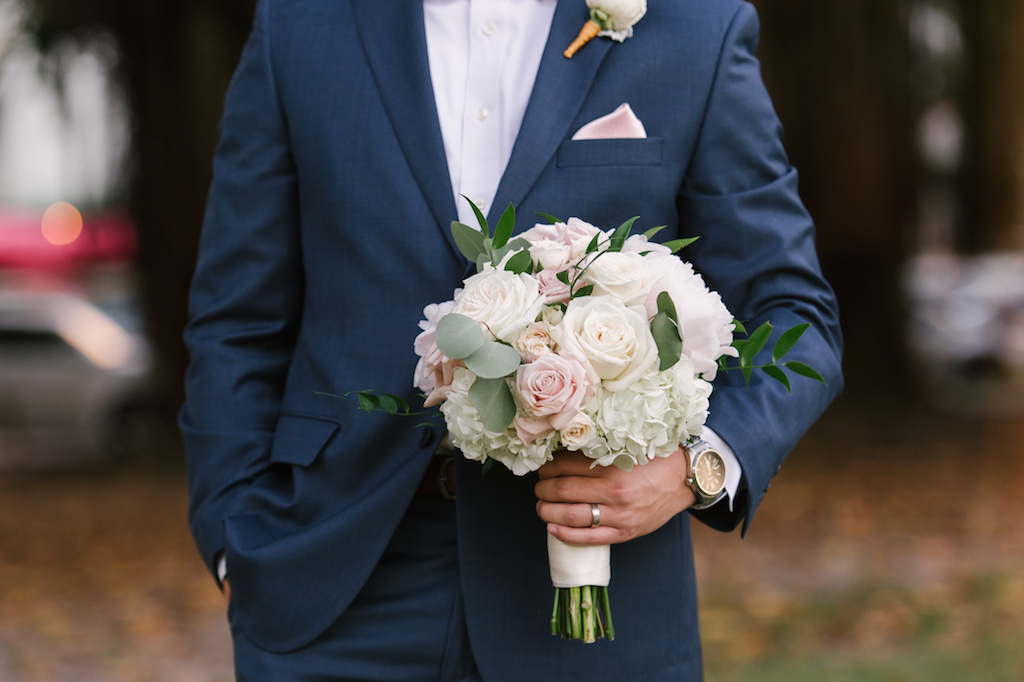 Groom in Navy Blue Suit with Blush Pink Pocket Square and White Rose Boutonnière, holding Blush and Ivory Rose with White Hydrangea and Greenery Bouquet