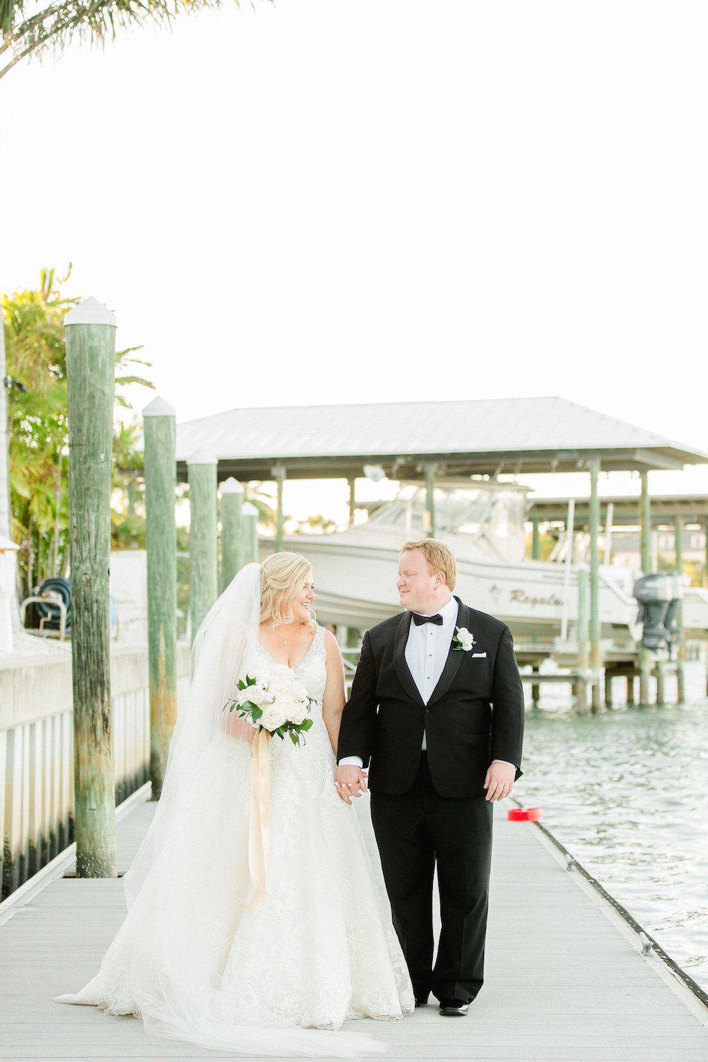 Waterfront Marina Outdoor Wedding Portrait, Bride in Morilee by Madeline Gardner Wedding Dress with White Rose and Greenery Bouquet with Long Gold Ribbon, Groom in Tux with White Floral Boutonnière | Clearwater Beach Wedding Venue The Carlouel Yacht Club | Tampa Bay Wedding Photographer Ailyn La Torre Photography