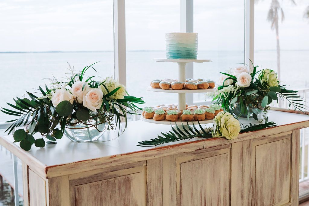 Elegant Tropical Coastal Blue and Green Wedding Reception Dessert Table with White and Blue Ombre Single Tier Round Wedding Cake and Light Blue and Seafoam Green Frosted Mini Doughnuts on Three Tiered White Cake Stand, with Natural Coastal Greenery and Blush Rose Flower Arrangements in Low Round Glass Vases | Tampa Bay Wedding Cake Bakery The Artistic Whisk