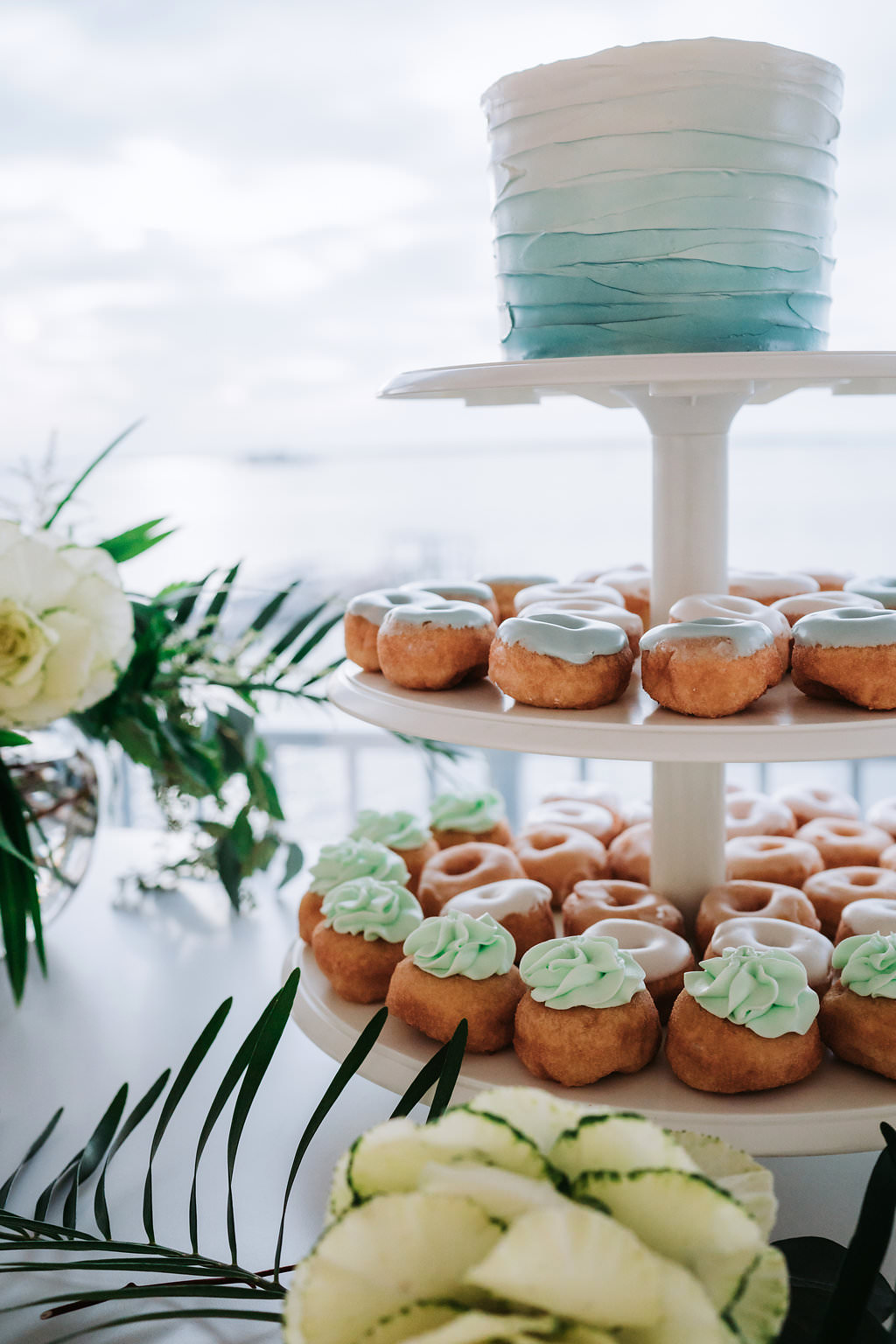 Elegant Tropical Coastal Blue and Green Wedding Reception Dessert Table with White and Blue Ombre Single Tier Round Wedding Cake and Light Blue and Seafoam Green Frosted Mini Doughnuts on Three Tiered White Cake Stand, with Natural Coastal Greenery and Blush Rose Flower Arrangements in Low Round Glass Vases | Tampa Bay Wedding Cake Bakery The Artistic Whisk