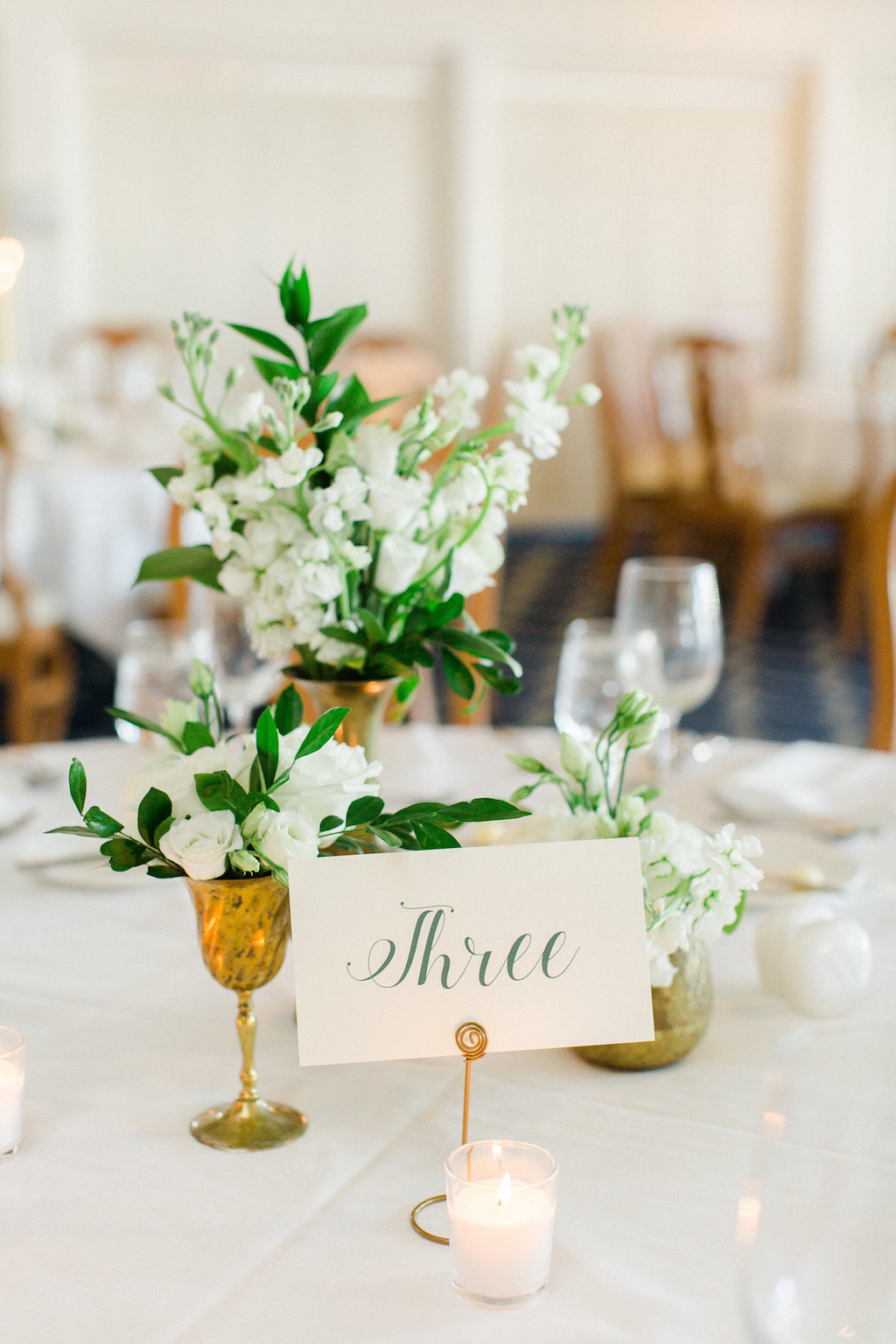 Old Florida Inspired Wedding Reception Table Decor with Small White Floral with Greenery Centerpieces in Mismatched Antique Gold Vases and Elegant Green on White Lettered Table Number Card | Tampa Bay Wedding Planner Glitz Events