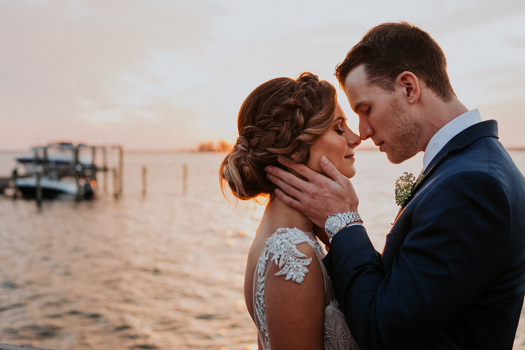 Outdoor Sunset Portrait on Waterfront Dock, Bride wearing Jeweled Lace Drop Back A Line Wedding Dress, Groom in Navy Suit with Silver Vest from Tampa Bay Formalwear Shop Nikki's Glitz and Glam | Dunedin, Florida Waterfront Wedding Venue Beso Del Sol Resort | Tampa Bay Wedding Photographer Grind and Press Photography | Hair and Makeup Femme Akoi