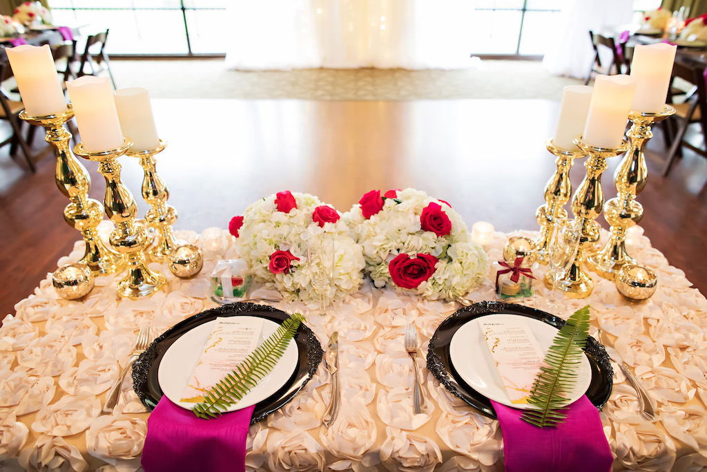 Ballroom Wedding Reception Sweetheart Table with Textured White Floral Linen, Low White Hydrangea and Red Rose Centerpiece, and Bold Stylish Gold Candlesticks, and Place Settings with Purple Napkins, Ferns, and Black Chargers | Tampa Bay Wedding Planner Special Moments Event Planning | Clearwater Wedding Florist and Rentals Gabro Event Services