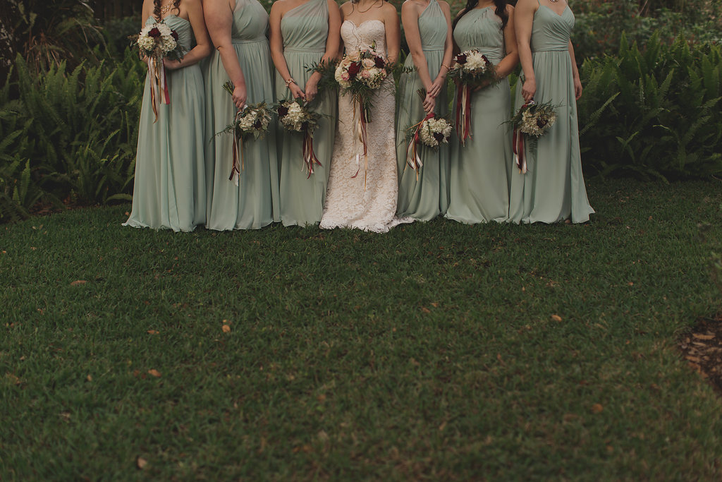 Outdoor Garden Bridal Party Portrait, Bride in Strapless A Line Floral Lace Stella York Wedding Dress, Bridesmaids in Mismatched Sage Green Floor Length Dresses, with Ivory, Blush, and Dark Red Bouquets with Greenery and Long Champagne and Maroon Ribbons | Tampa Bay Wedding Photographer Stacy Paul Photography