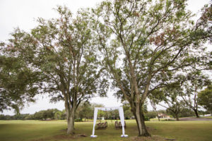 Outdoor Golf Course Wedding Ceremony Decor with Rectangular Arch with White Drapery and Hanging Flowers Under Large Tree | Clearwater Wedding Venue Countryside Country Club
