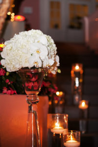 Outdoor Garden Courtyard Wedding Ceremony Decor with White Hydrangea and Orchid Flowers in Tall Glass Vase with Floating Votive Candles in Hurricane Lanters