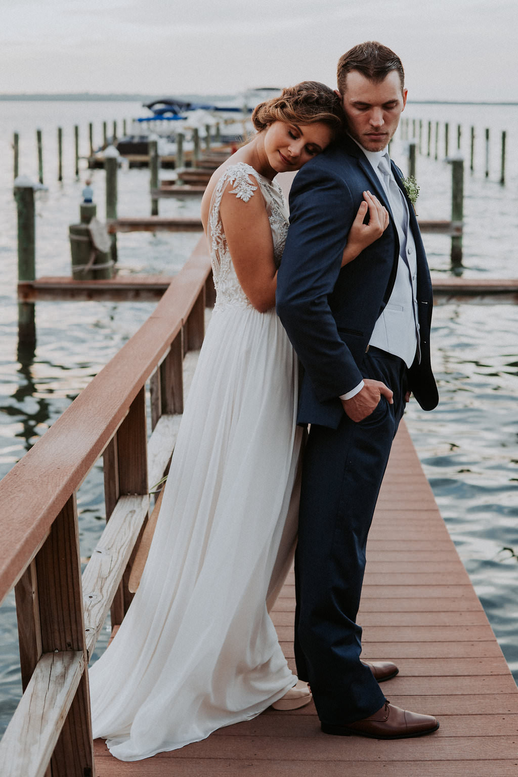 Outdoor Portrait on Waterfront Dock, Bride wearing Jeweled Lace Drop Back A Line Wedding Dress, Groom in Navy Suit with Silver Vest from Tampa Bay Formalwear Shop Nikki's Glitz and Glam | Dunedin, Florida Waterfront Wedding Venue Beso Del Sol Resort | Tampa Bay Wedding Photographer Grind and Press Photography