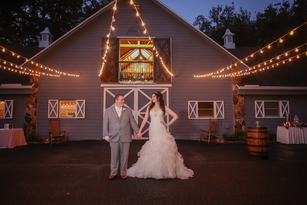 Outdoor Nighttime Bride and Groom Barn Wedding Portrait, Bride in Strapless Jeweled Mermaid Wedding Dress, Groom in Gray Suit with Blush Tie with Antique Barrels and String Lights | Tampa Wedding Photographer Lifelong Studios Photography | Rustic Barn Venue Lange Farm