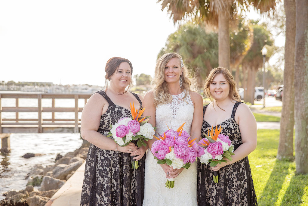 Outdoor Waterfront Bridal Party Portait, Bride in Lace Illusion Neckline Essence of Australia Wedding Dress, Bridesmaids in Black Floral Lace Dresses, with Pink Peony, White Hydrangea, Orange Bird of Paradise and Greenery Bouquet | Downtown St Pete Waterfront Historic Wedding Venue The St Petersburg Museum of History | Tampa Bay Wedding Photographer Kristen Marie Photography