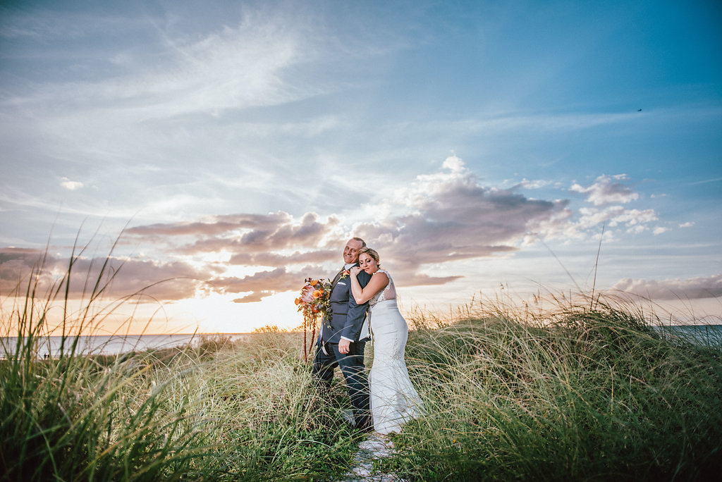 Outdoor Waterside Sunset Bride and Groom Wedding Portrait with Gold and Red Bouquet with Greenery and Ribbon | Clearwater Beach Wedding Planner Special Moments Event Planning