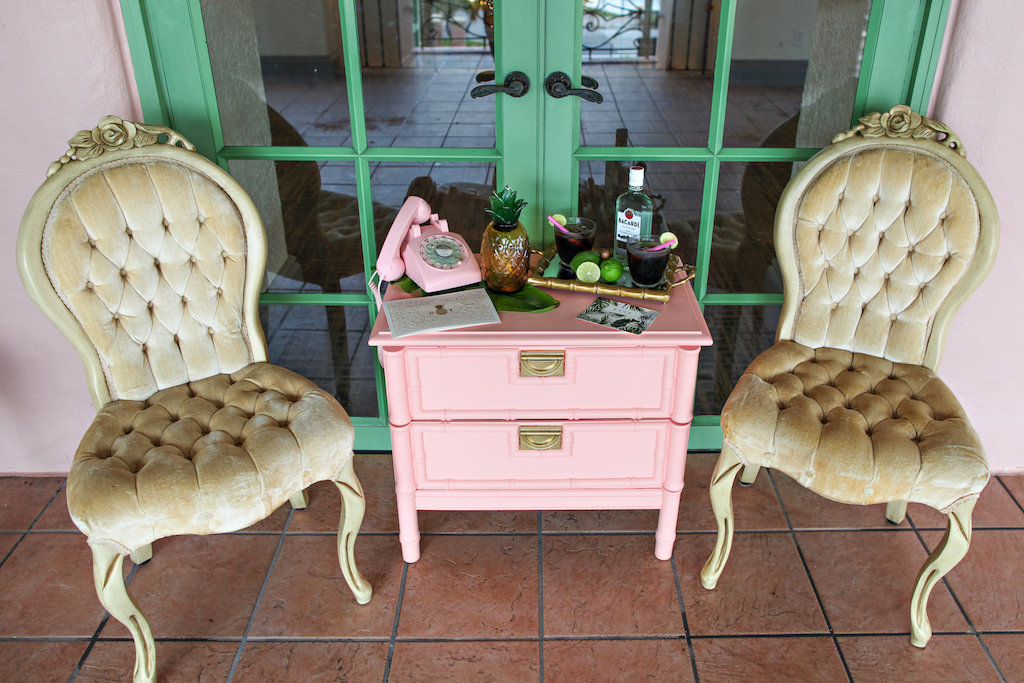 Hotel Courtyard Old World Havana Inspired Wedding Reception with Tan Velvet Chairs, Pink Table with Rotary Phone, Pineapple Decor and Rum Cocktail Setup | Vintage Rentals by St. Pete A Chair Affair