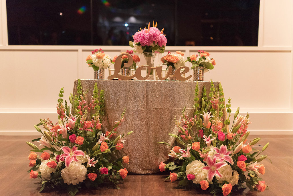 Tropical Old Florida Themed Wedding Reception Decor Bride and Groom Sweetheart Table with Orange and Pink Rose, Pink Lily, White Hydrangea and Greenery Flowers with Medium and Small Pink Peony Centerpieces in Mercury Glass Silver Jars with Sparkling Gold Linen and Oversized Stylish Love Sign