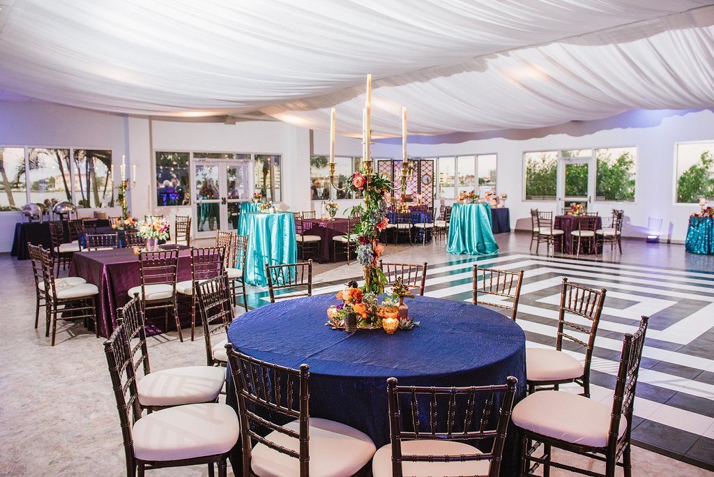 Whimsical Jewel Tone Wedding Reception with Amethyst, Midnight, and Emerald Linens, and Tall Candelabra with Hanging Flowers and Greenery Centerpiece and White Ceiling Draping and Wooden Chiavari Chairs | Tampa Bay Wedding Rentals Over the Top Linens | Clearwater Wedding Planner Special Moments Events Planning | Indoor and Outdoor Wedding Waterfront Reception Venue Clearwater Beach Recreation Center