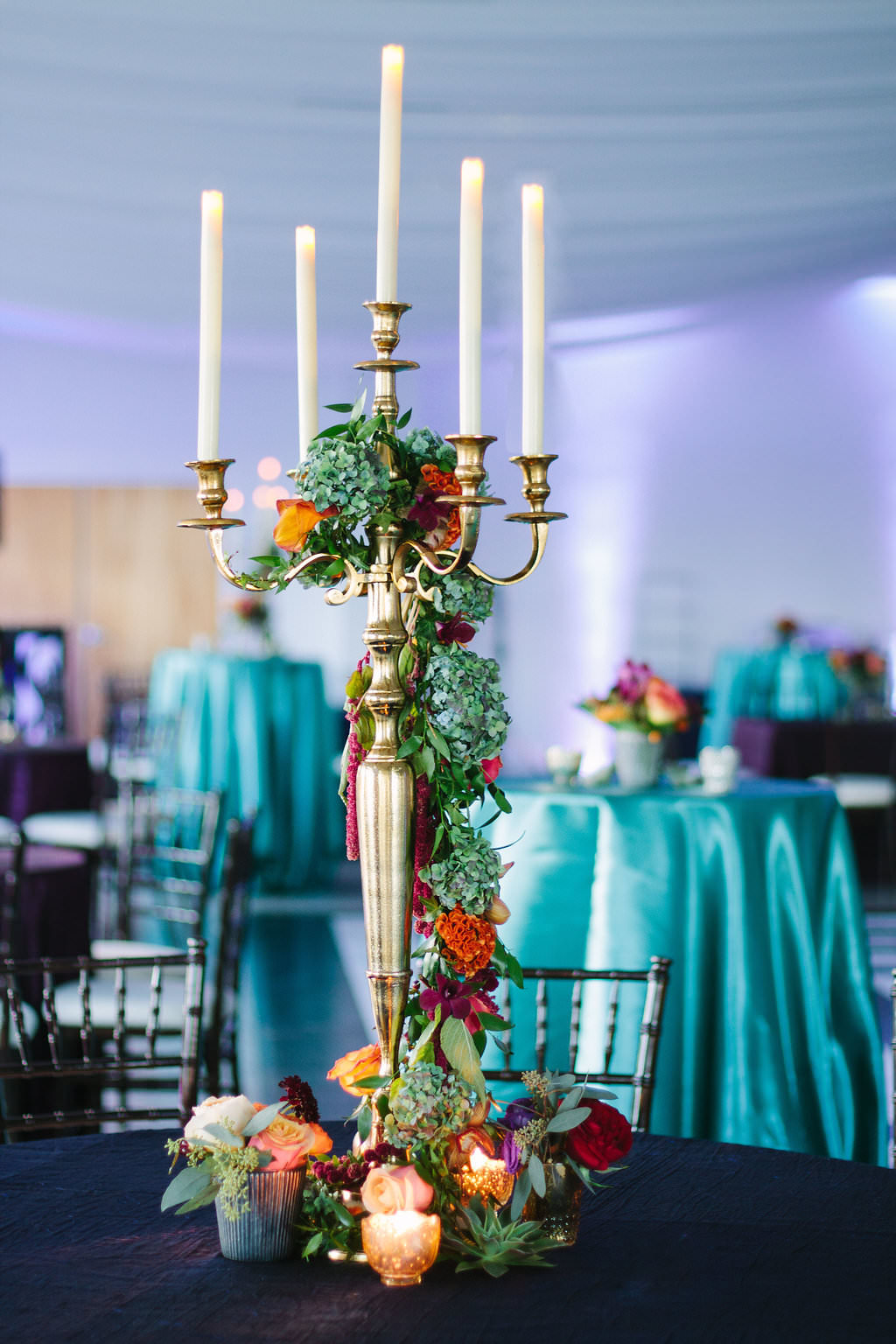 Jewel Tone Whimsical Wedding Reception Decor with Tall Gold Candelabra with Hanging Red, Purple, and Yellow Florals with Greenery, and Midnight Blue and Emerald Green Linens | Tampa Bay Wedding Planner Special Moments Events Planning | Clearwater Wedding Rentals Over The Top Linens