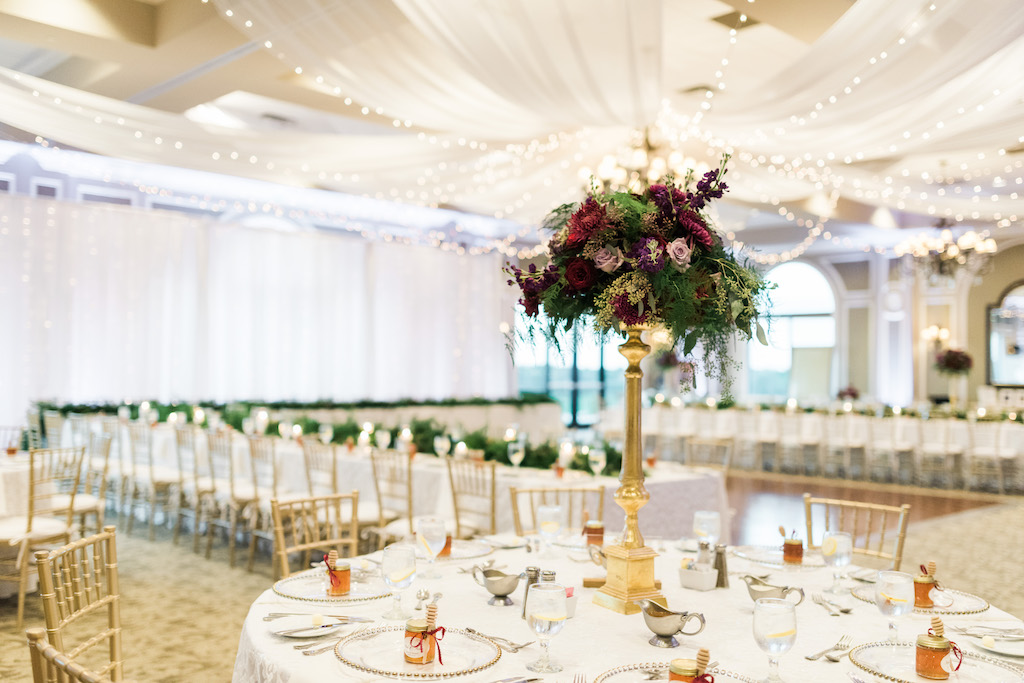 Whimsical Ballroom Wedding Reception Round Table Decor with Honey Jar Wedding Favors, Gold Chiavari Chairs, Tall Magenta and Purple with Greenery Centerpiece in Tall Gold Vase, and White Ceiling Draping with String Lights | Sarasota Ballroom Wedding Reception Venue Lakewood Ranch Golf and Country Club