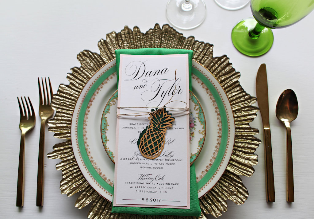 Old World Havana Tropical Inspired Wedding Reception Table Setting with Gold Charger, Vintage China Plates, Brushed Gold Flatware, Green Satin Linens and Laser-cut Pineapple Menu with Twine, and Colored Drinking Glasses | Tampa Bay Wedding Rentals A Chair Affair