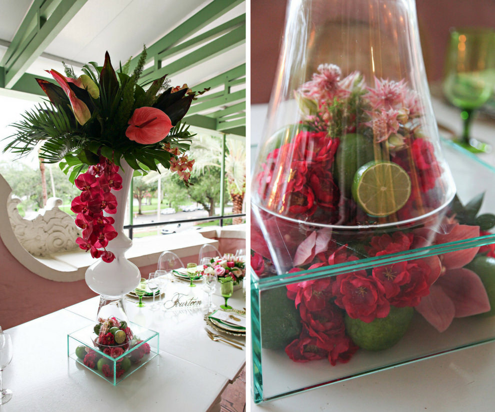 Hotel Courtyard Old World Havana Inspired Wedding Reception Extra Tall Centerpiece with Magenta Orchids and Pink Lilies, Tropical Fern and Palm Frond Greenery, in White Glass Vase on Clear Glass Vase Filled with Fruit, Limes and Florals