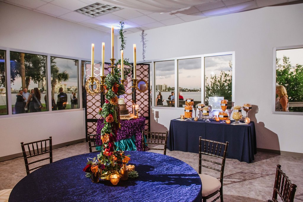 Whimsical Jewel Tone Wedding Reception Decor with Tall Candelabra Centerpiece with Hanging Garland Orange and Red Florals with Greenery and Small Gold Tealight Candles on Midnight Blue Linen, with Purple and Emerald Green Linen Dessert Table and Popcorn Bar | Tampa Bay Wedding Cake and Dessert Bakery A Piece of Cake